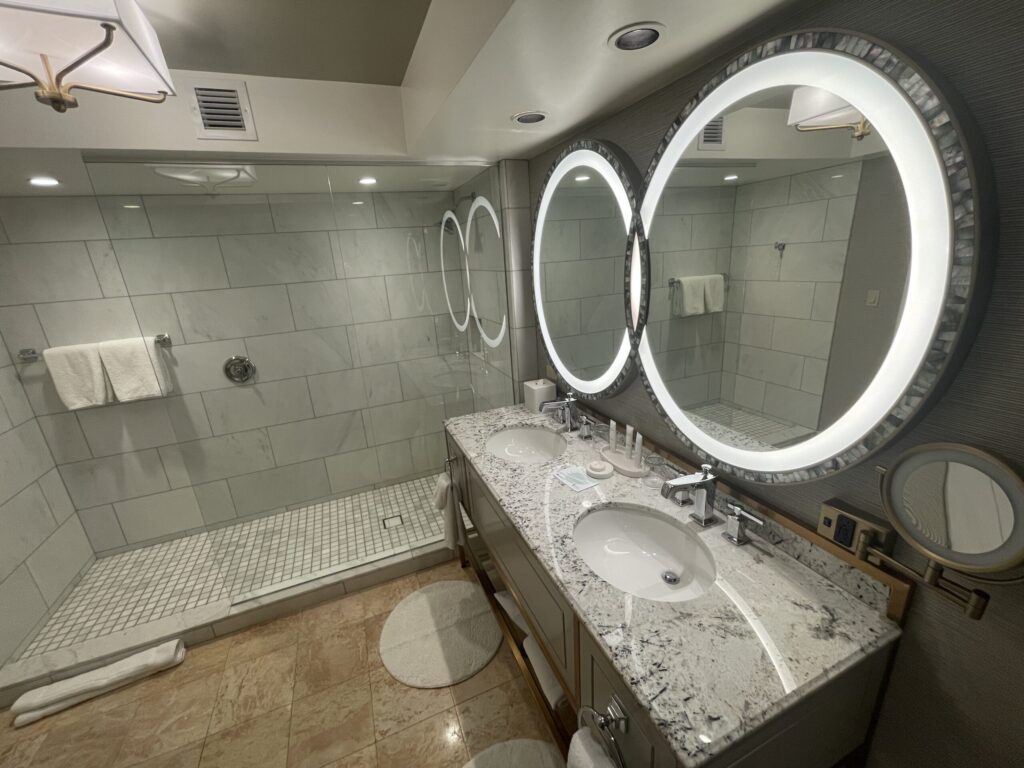 The glass shower is pictured behind the dual sink vanity.