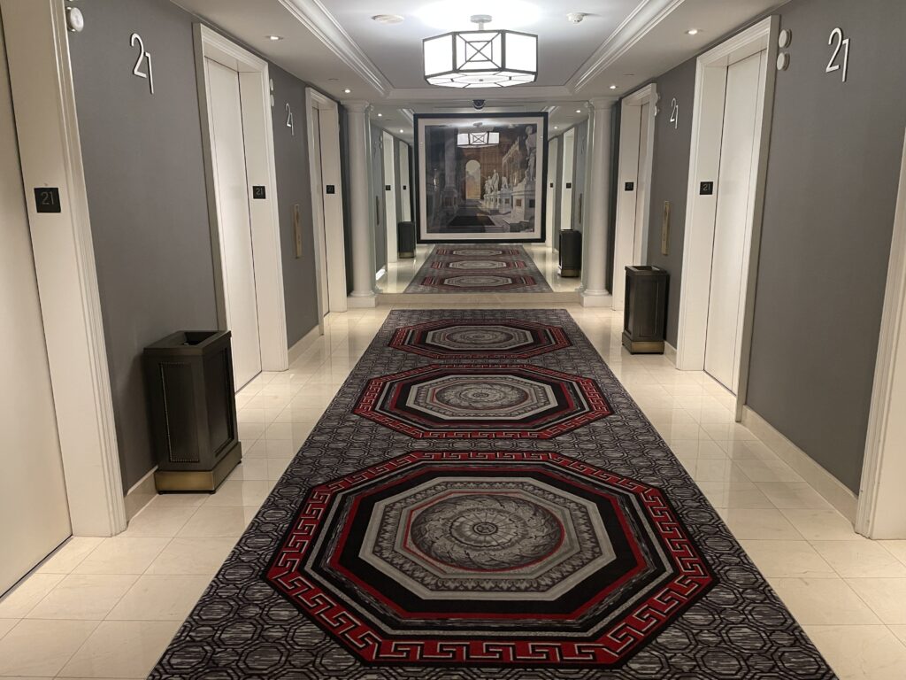 An elevator lobby in Caesars Palace's Palace Tower that has an intricately designed carpet and is well lit. 