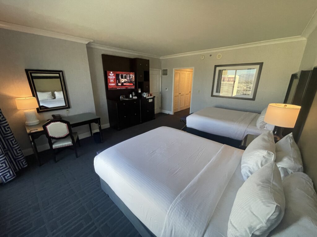 Beds facing a TV stand. A work desk and chair are to the left of the TV.