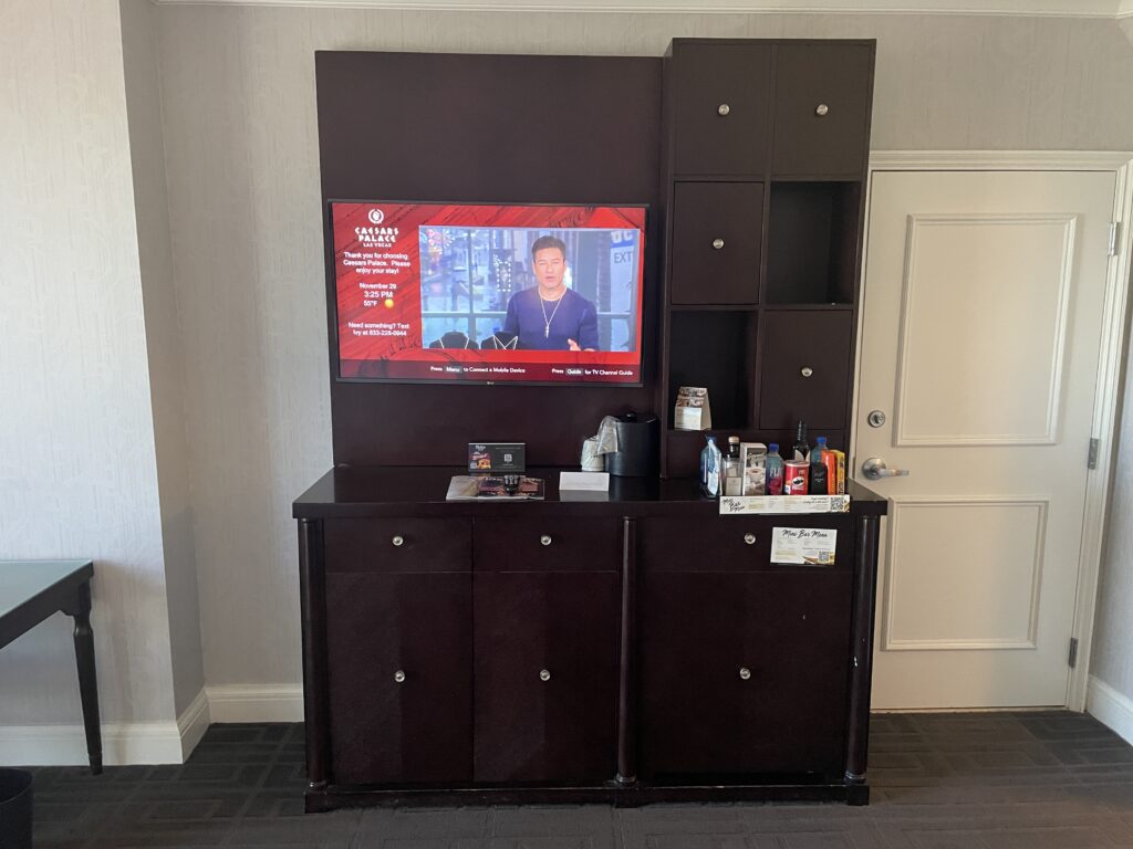 TV stand with a TV turned on and mini bar items displayed atop the counter. 