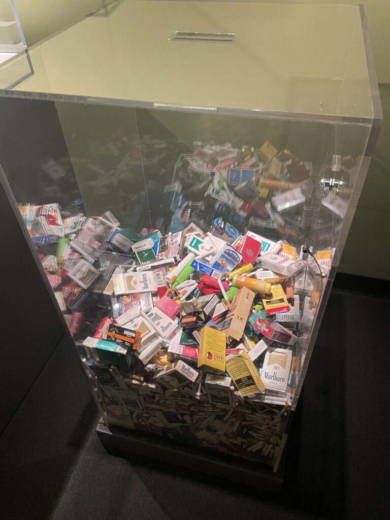 A large clear plastic bin half filled with packs of cigarettes. 
