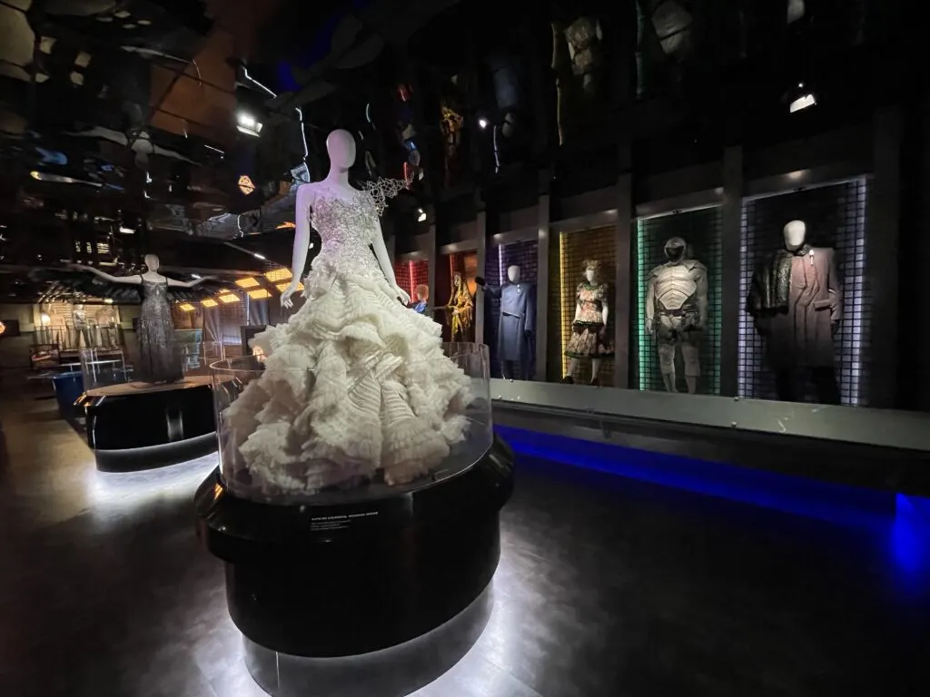 Katniss' Wedding dress is featured prominently on a podium in the middle of a room full of costumes. 