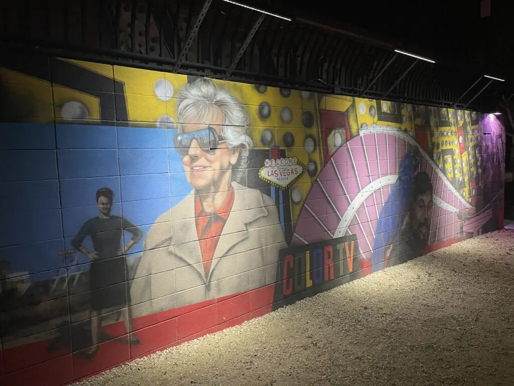 Betty Willis wearing sunglesses is depicted on the mural next to a small image of her "Welcome to Fabulous Las Vegas" sign. 