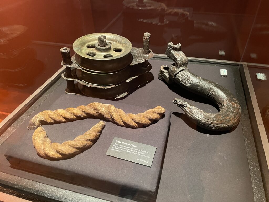 A section of rope, a metal hook, and pully in a display case. 