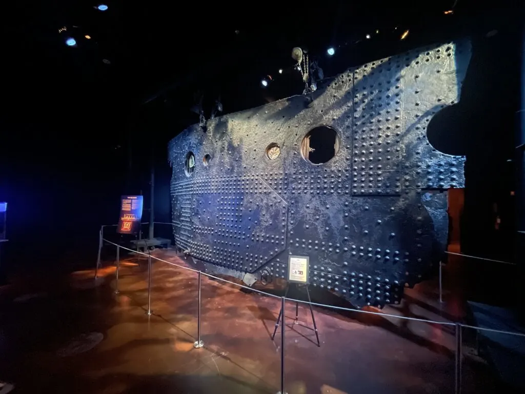 A large section of titanic's hull hangs vertically from the ceiling.