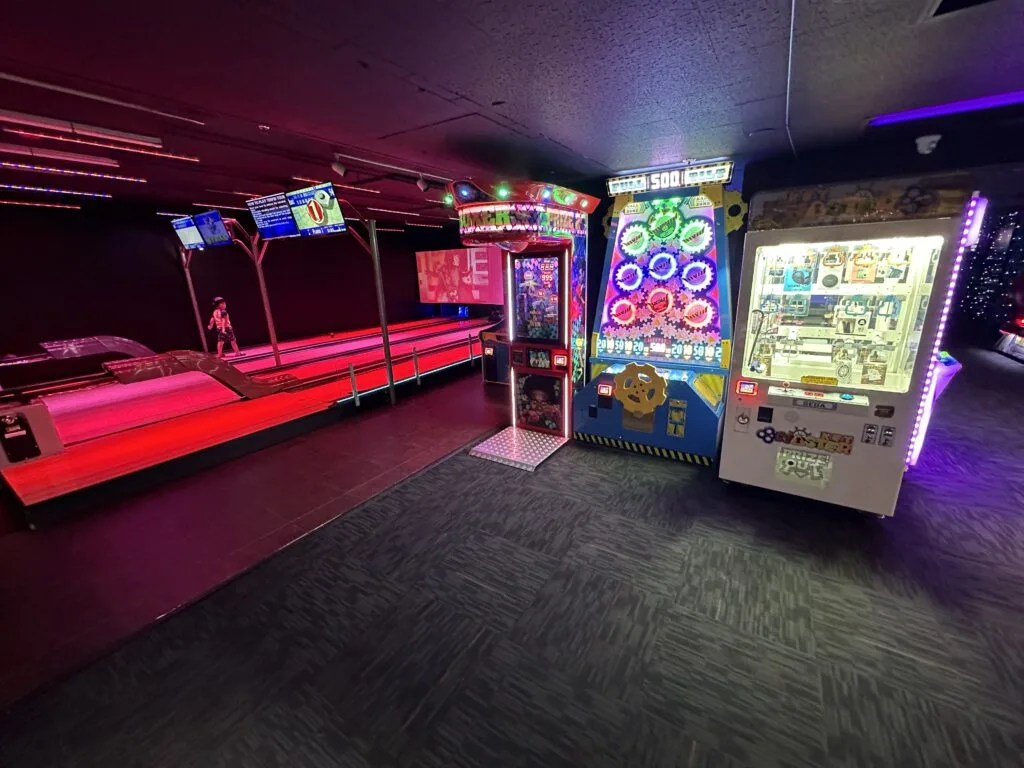 Several arcade games are lined up along a wall, and a few bowling alleys are in the background.