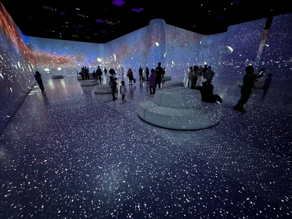 The Milky Way, stars, and rocks floating through space are depicted on the screens around the room. 