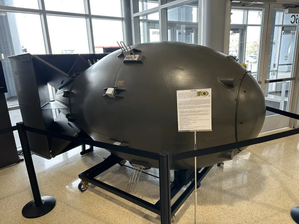 A large green oval shaped bomb with a square fin on the tail end designed to look like Fat Man.