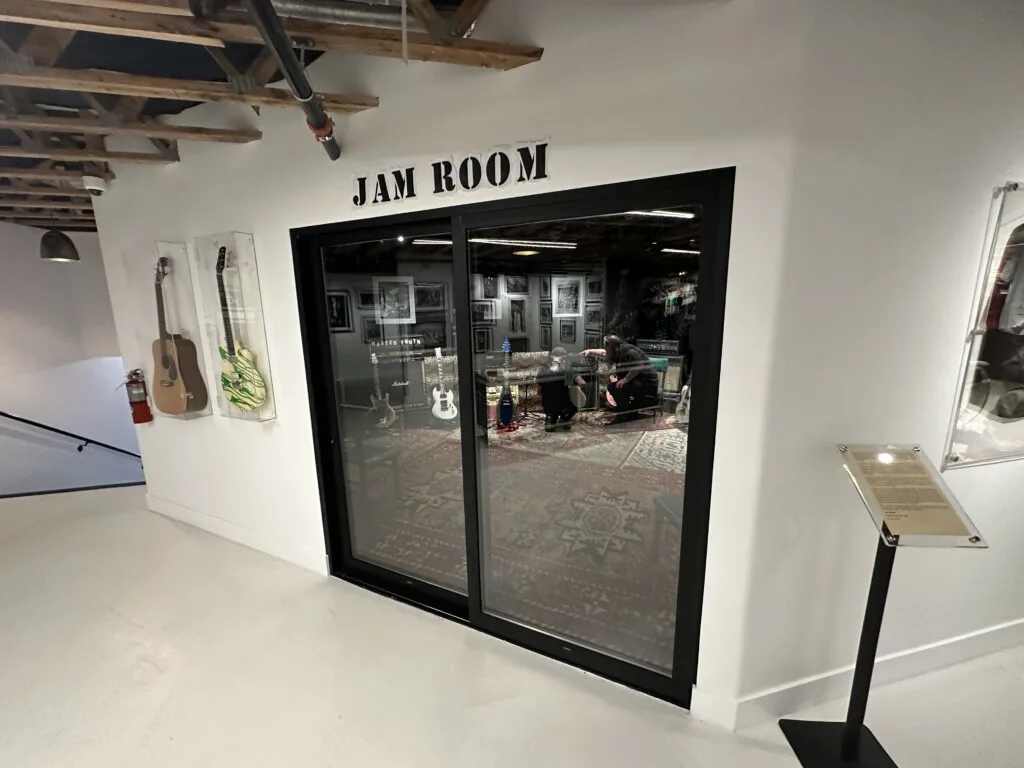 The doors that lead into the Jam Room at The Punk Rock Museum. Through the glass doors, you can see two individuals adjusting instruments. 