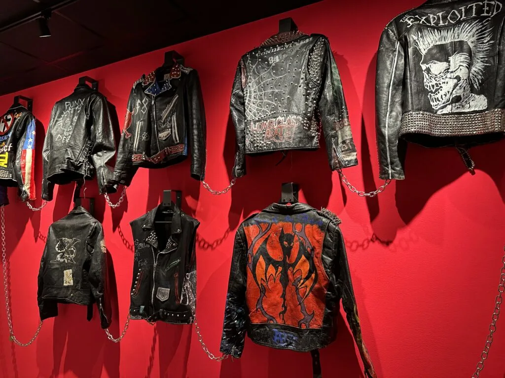 Band worn leather jackets with unique artwork hanging from a wall and chained together.
