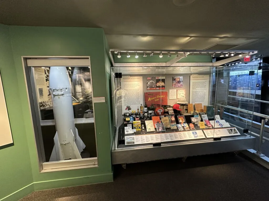 A number of items on display behind glass that demonstrate how the bomb had infiltraded popular culture like magazines, comics, cocktail mixes, and toys. 