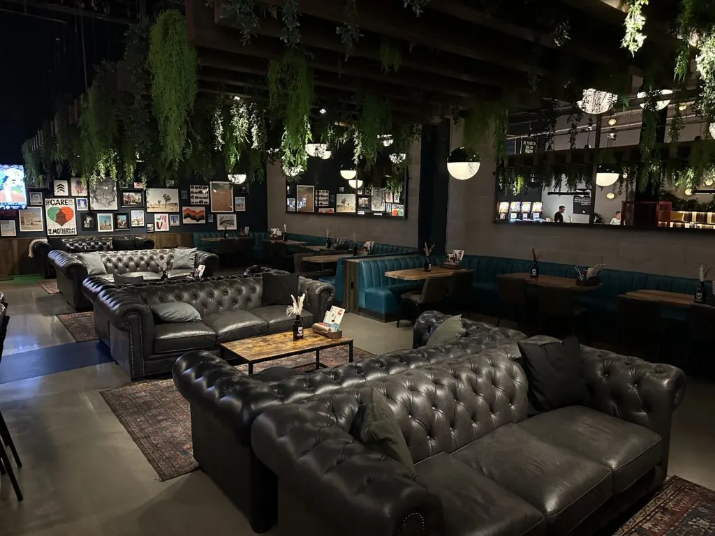 Leather seating and tables underneath a ceiling that is made of green plants. 