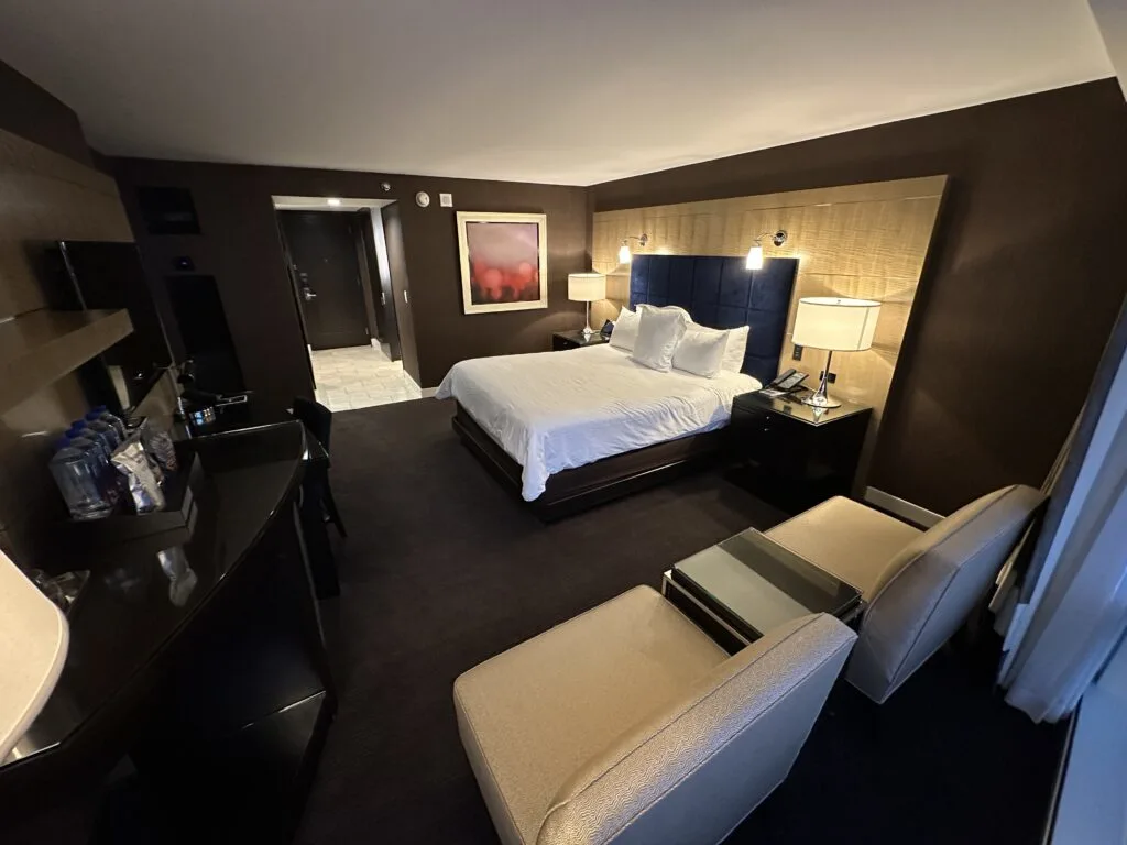 Another angle of the Deluxe King room at Aria that shows the bed, and 2 white chairs in the foreground. 