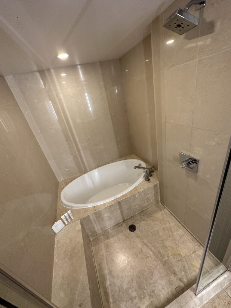A tan marble shower positioned next to a white oval shaped bathtub. 