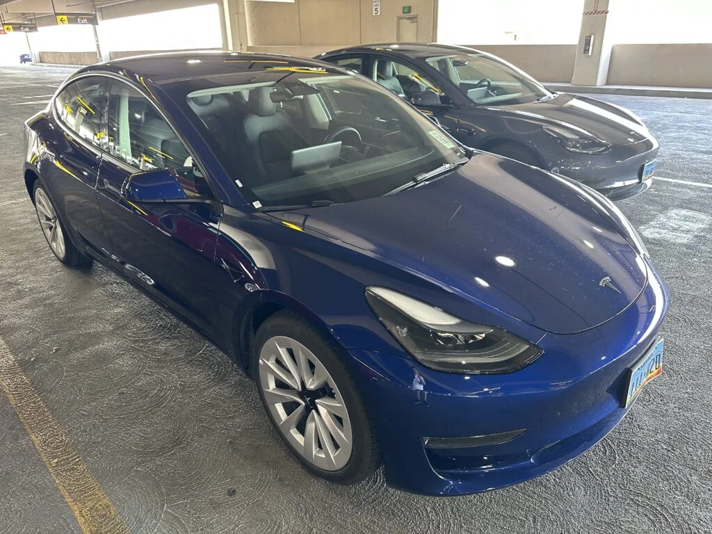 A blue Tesla Model 3 parked in a lot next to another Tesla.