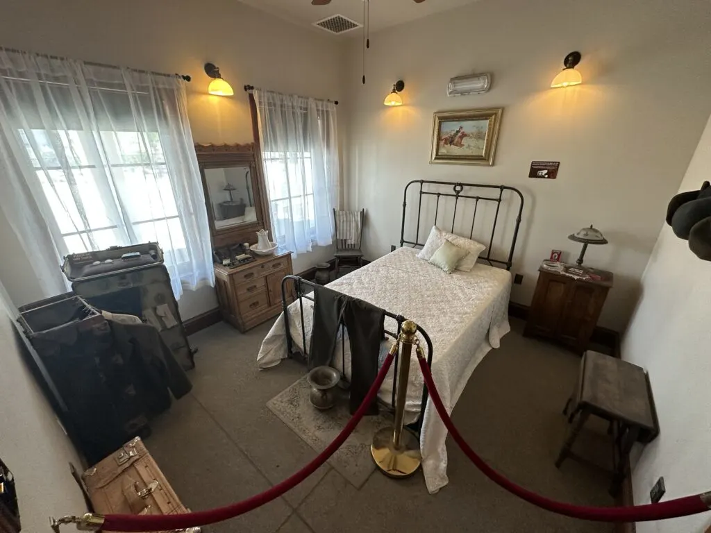 Inside a hotel room at the Lincoln Hotel that has a small twin bed, dresser, and several light fixtures.