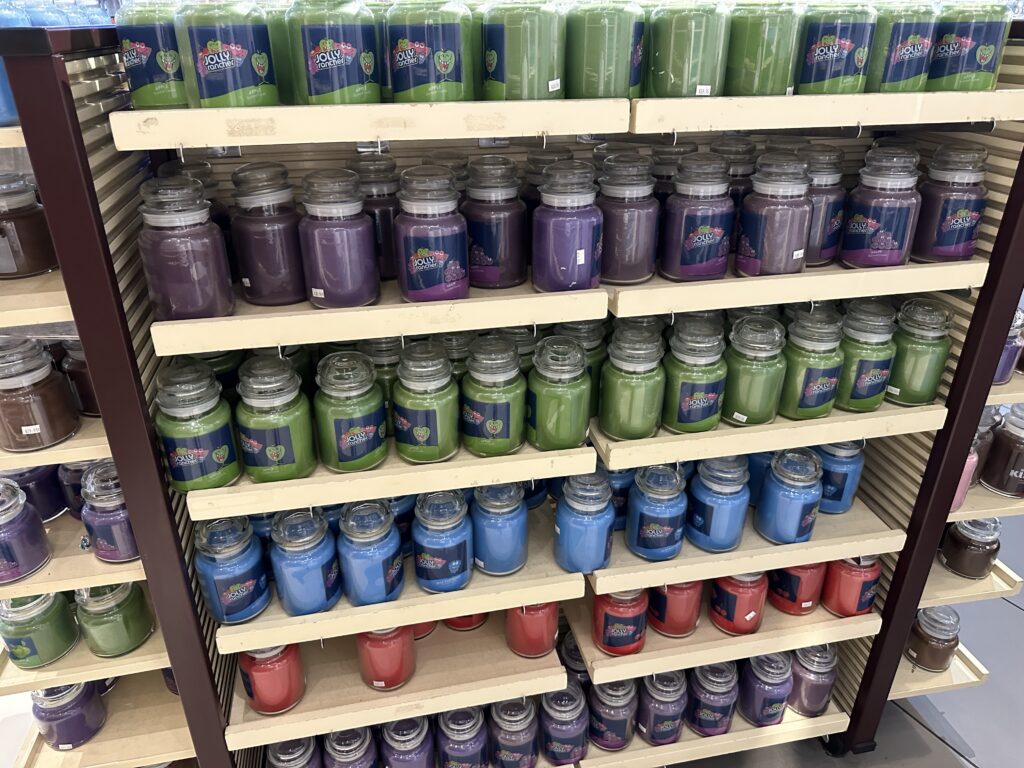 A shelving unit stocked with glass candles scented like various Jolly Rancher flavors. 