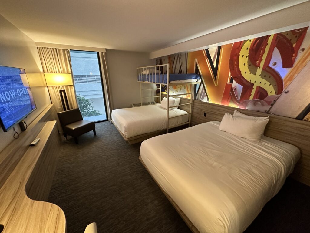 A wide angle photo of the room with 2 queen beds and one twin lofted above the far bed.