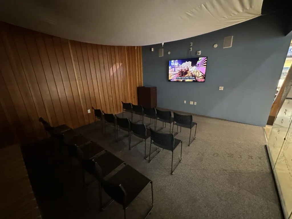 A room with about 15 chairs facing a TV screen that is playing an informational video. 