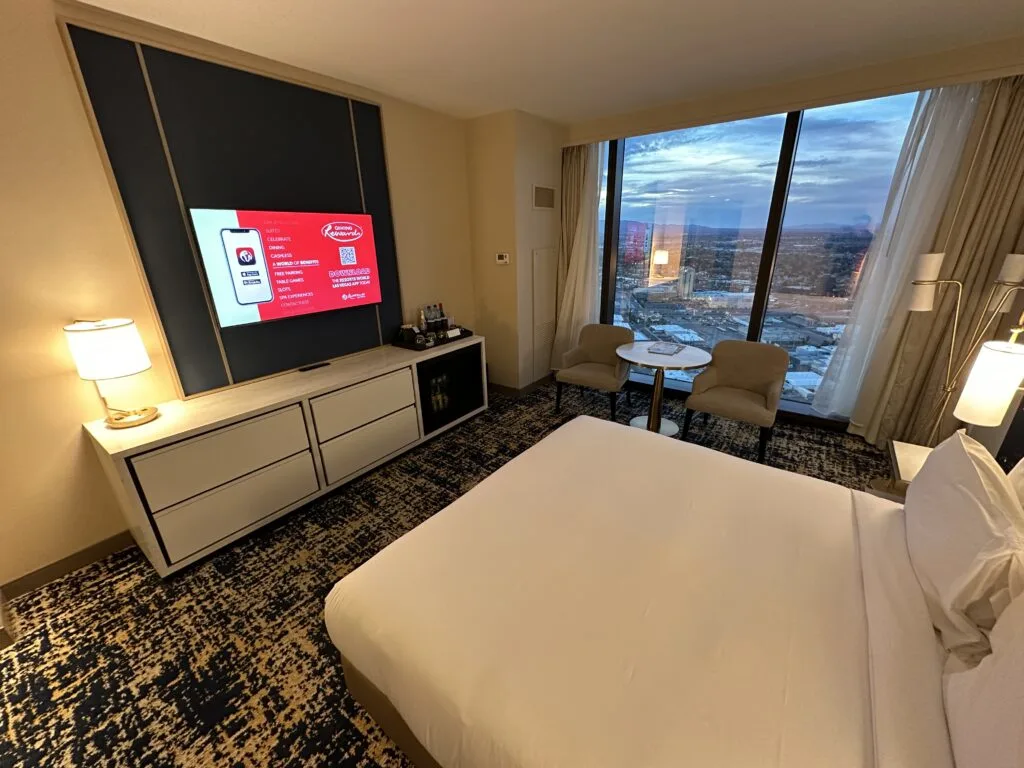 A wide angle photo of the foot of the king bed, TV, and window overlooking las Vegas. 