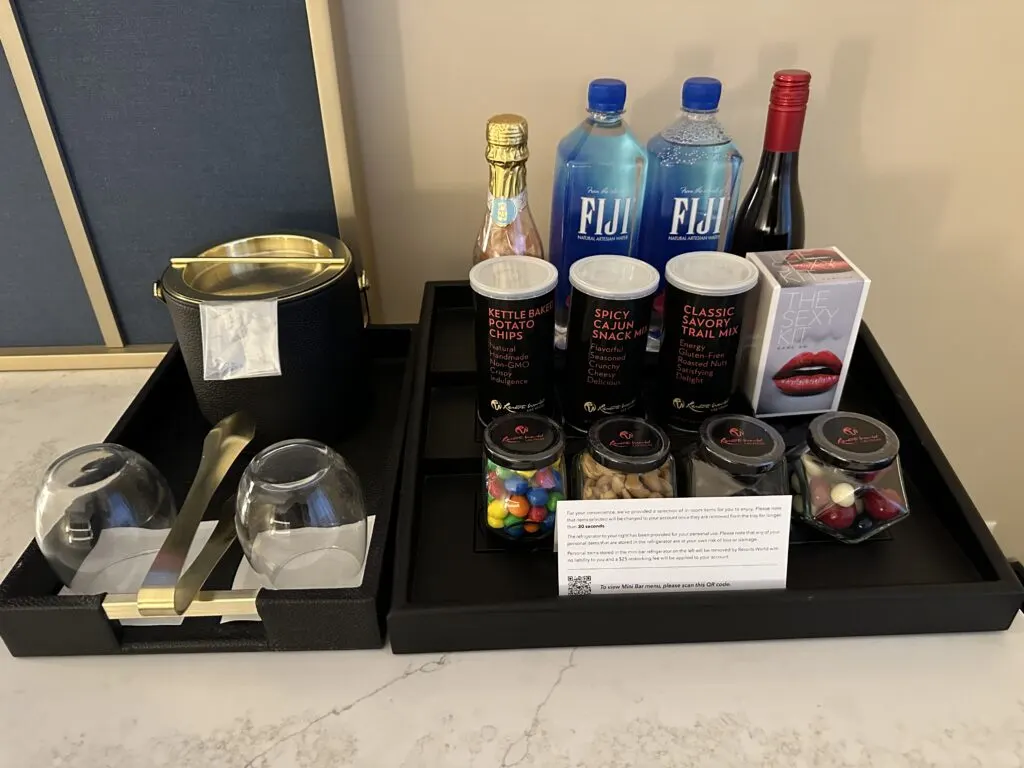 Countertop mini bar stocked with fiji water and snacks. Alongside it are two glasses and an ice bucket. 