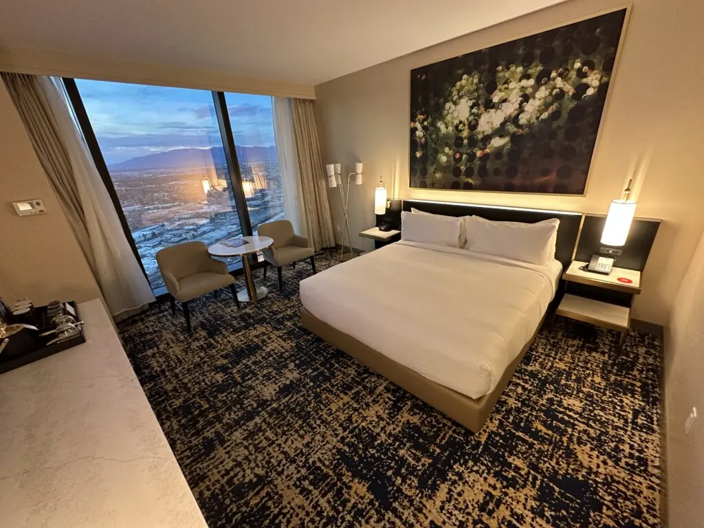 A wide angle photo of the king bed flanked by end tables. Above the bed is a large abstract painting. 