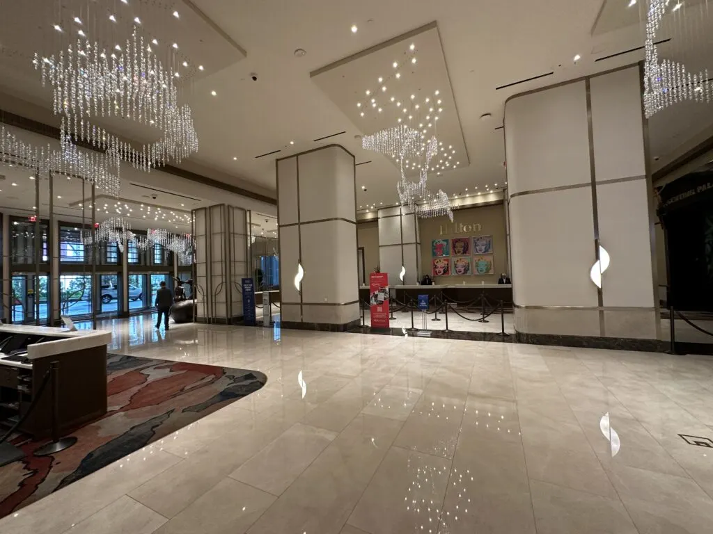 Hilton hotel lobby at Resorts World which features light brown marble on the floor and decorative chandeliers on the ceiling. 