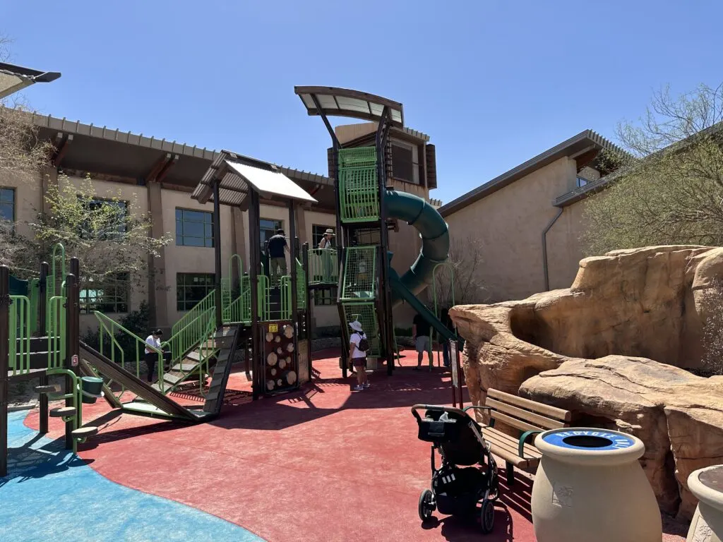 A green and purble play structure reaches a height of about 2 stories. A long spiral slide decends from the top to the ground level. 