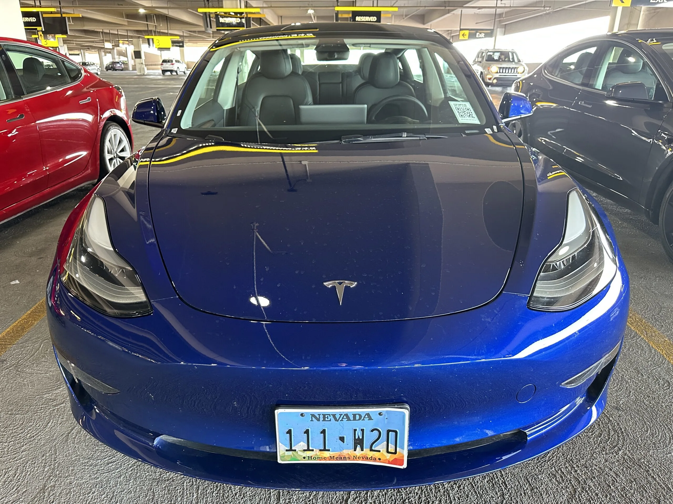 A blue Tesla Model 3 is photographed from head on.
