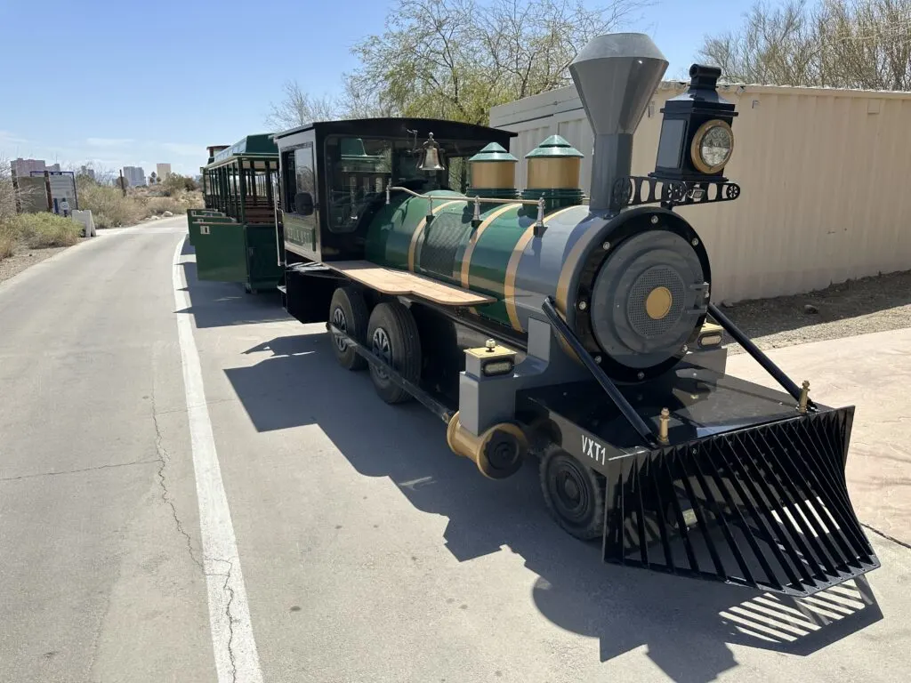 A green freight train with wheels to drive on a road surface is loading up with new passengers.