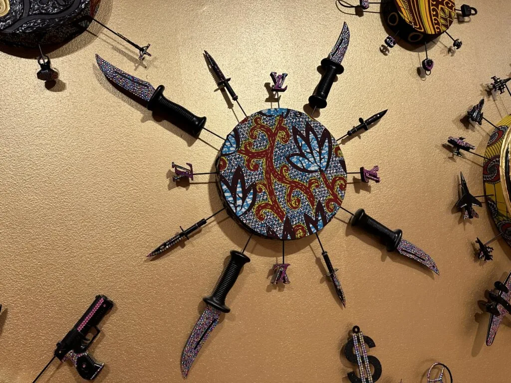 A decorative circle hanigng on the wall with knives radiating from it like rays of the sun. 