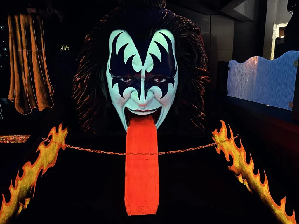 A huge band member face with tounge extended glowing under the black light. The tounge doubles as a ramp to hit your ball up into the mouth.