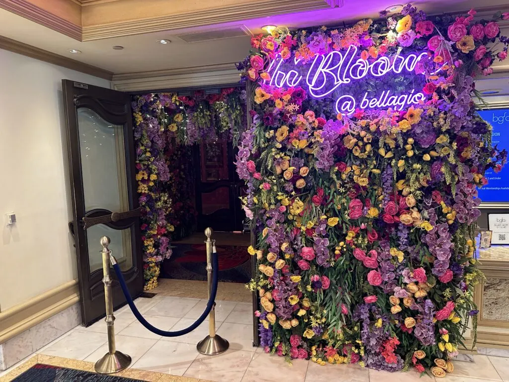 Entrance to the gallery, which is covered in faux flowers and plant life. Nestled in the fake flowers is a purple neon sign that says "In Bloom @ Bellagio".