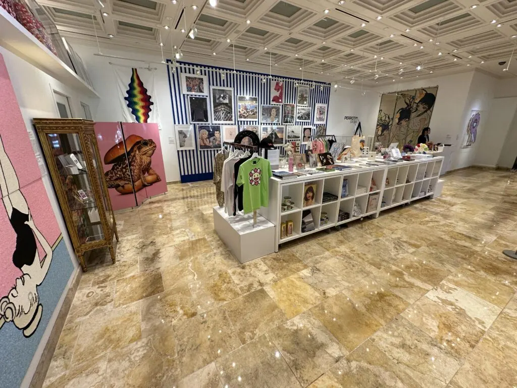 Gift shop just outside the art gallery which has photographs, paintings, shirts, and books on display.