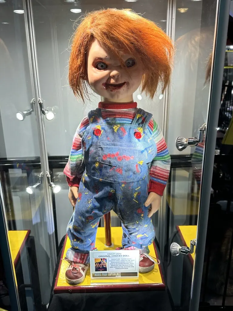 Chucky the doll stands in a glass case.