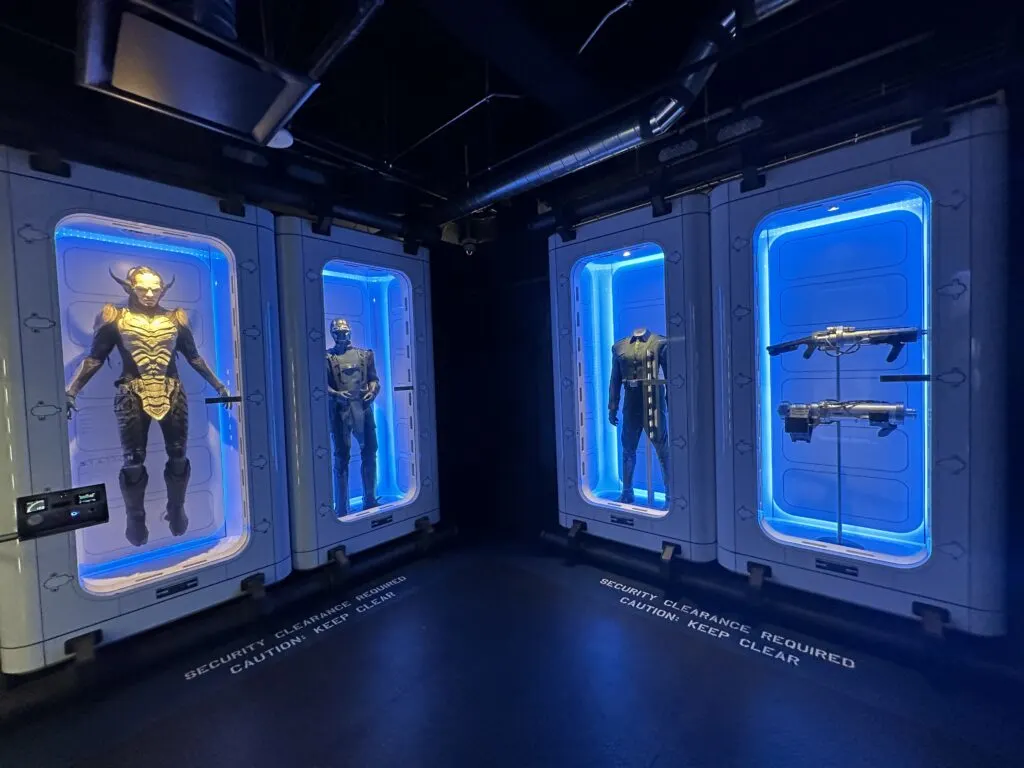 Movie props and superhero suits on display in illuminated glass cases. 