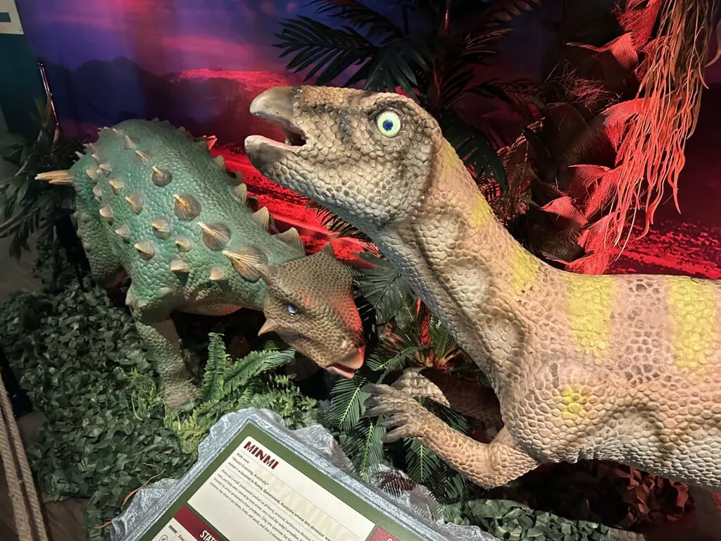 2 different types of dinosaurs standing next to eachother. The one in the foreground is on his hind legs and has a startled look on his face.