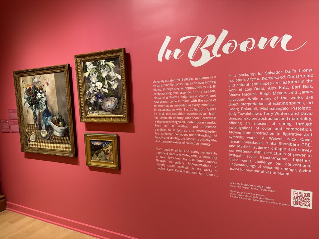 3 floral paingings hang next to a written introduction to the gallery. 