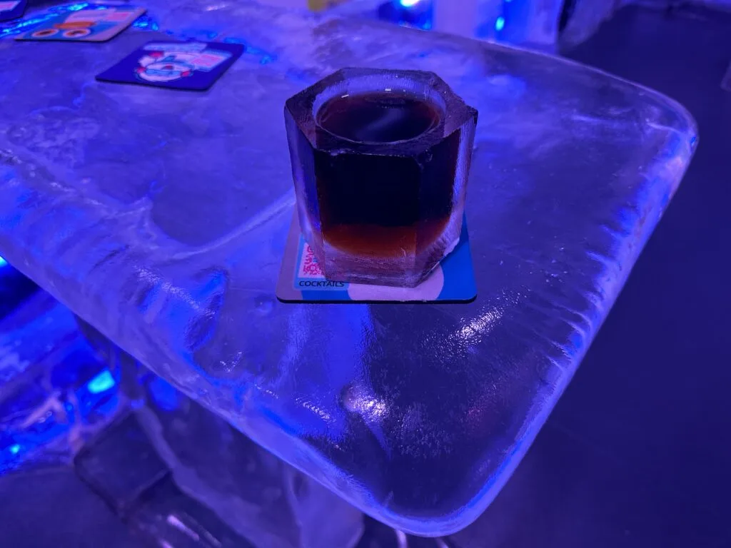 A rum and coke in a glass made of Ice and sitting on a table made of ice. 