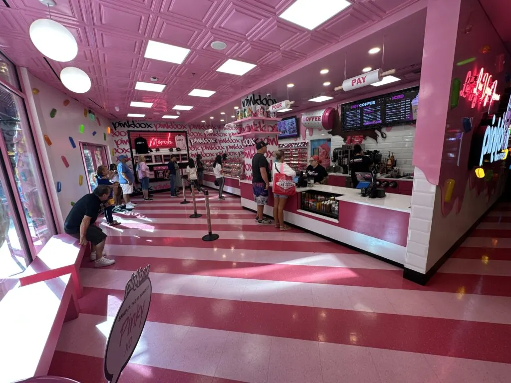 A wide angle picture of the  doughnut shop which has a pink and white striped floor, pink walls, and a pink ceiling. 