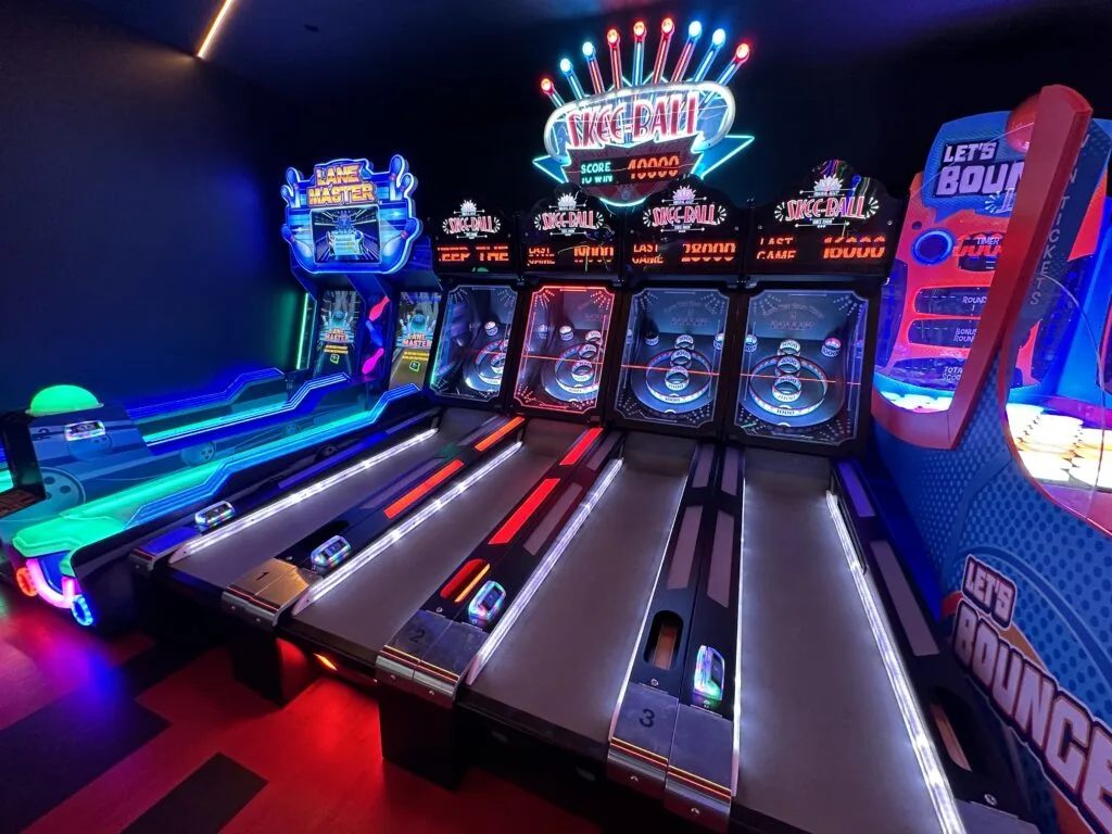 A row of skee ball games next to a couple of simulated bowling games. 