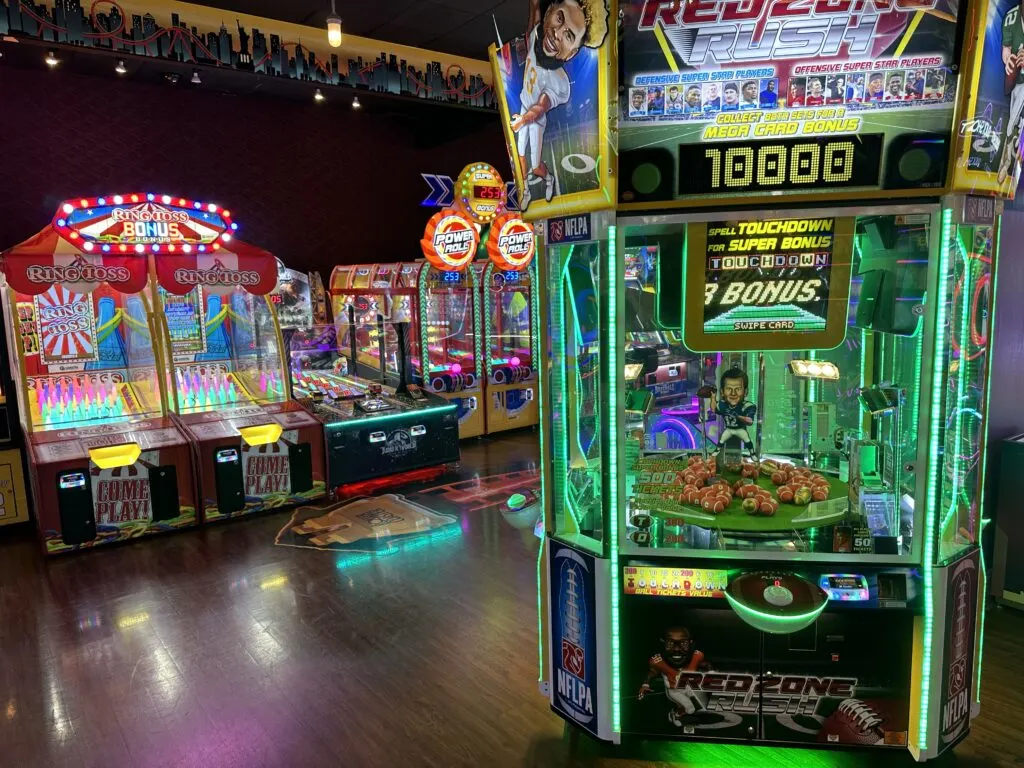 A football themed arcade game sits in the foreground and additional games are along a wall in the background. 