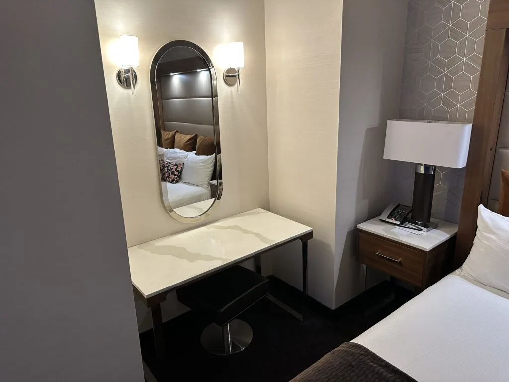 A well lit powder desk with a bench, desk, and mirror above. 