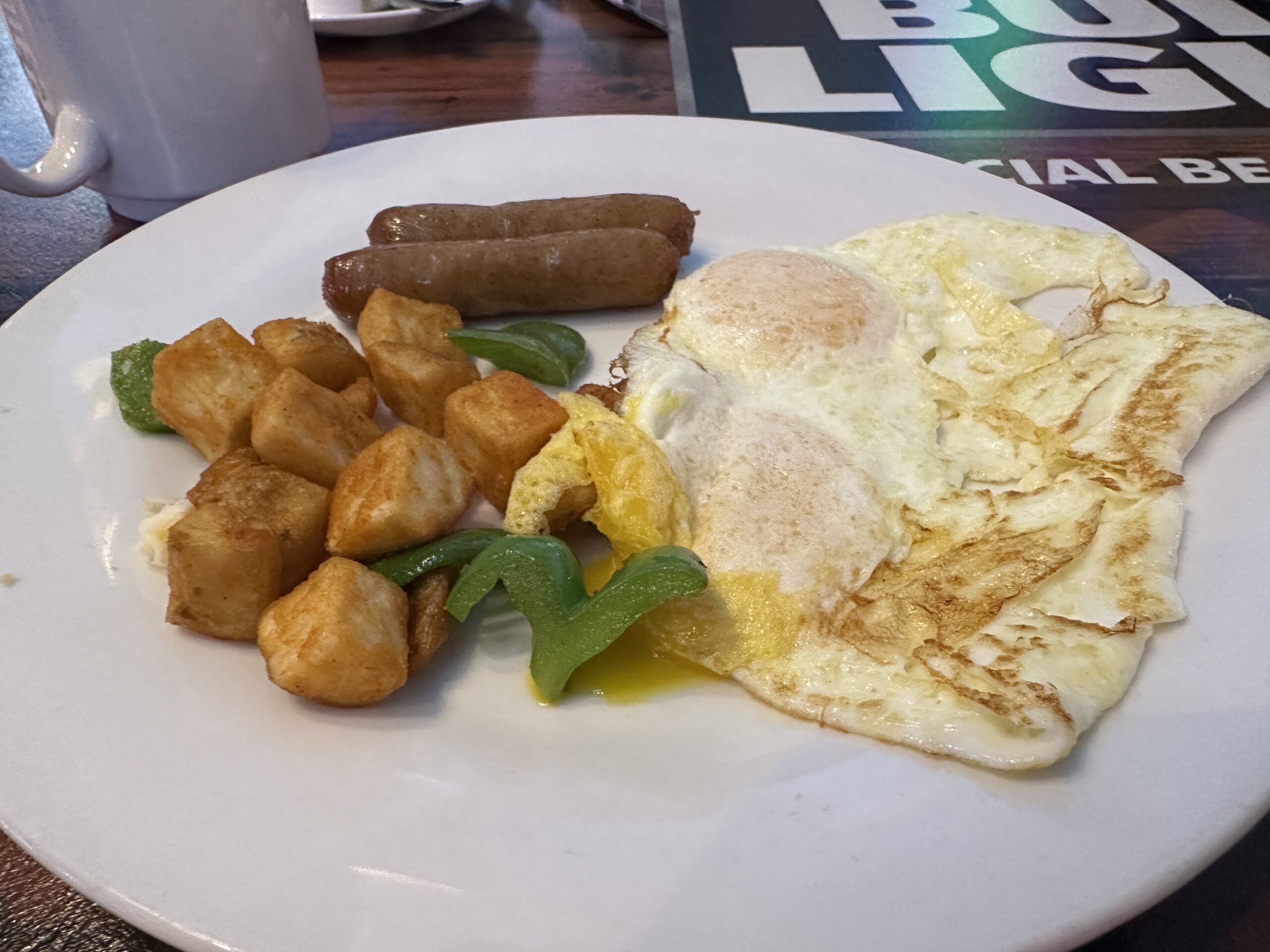 A white plate with a very small pile of breakfast potatoes, 2 links of sausage, and 2 eggs over easy.