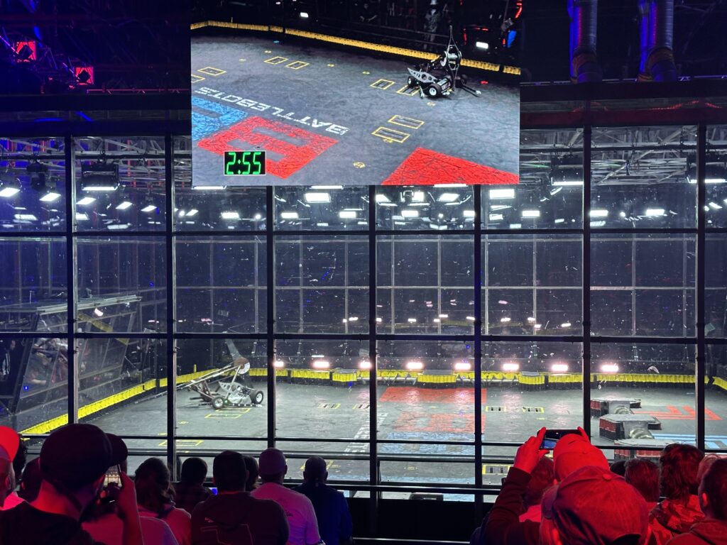2 robots fight in the corner of the Battlebots Arena. 