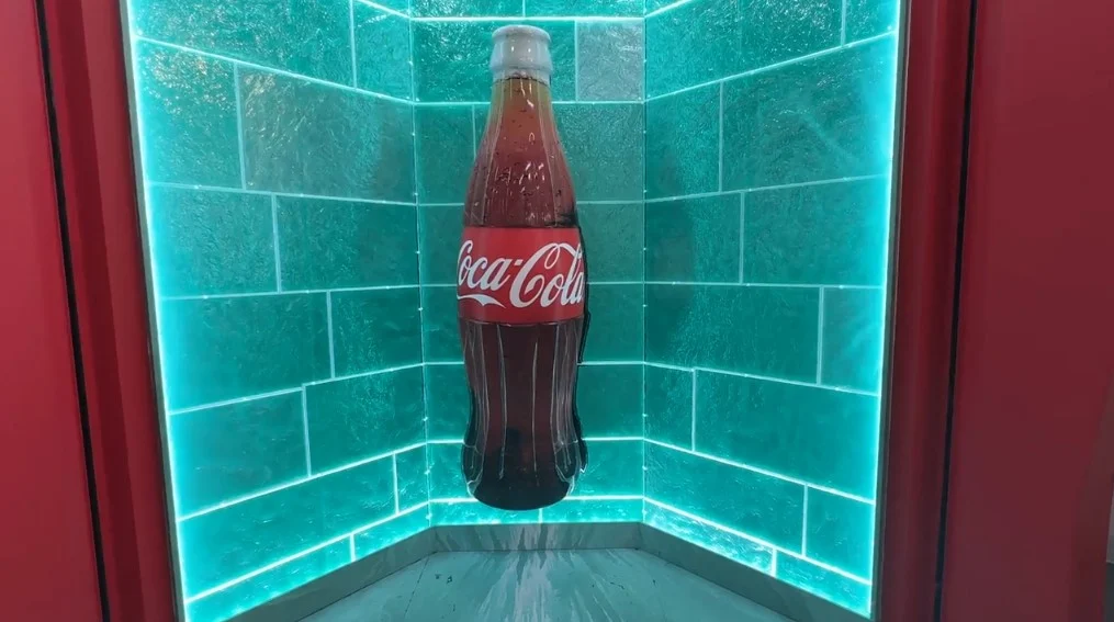 A photo opportunity at the Coca Cola store, with an illuminated back wall and a giant glass bottle of Coke in the middle. 