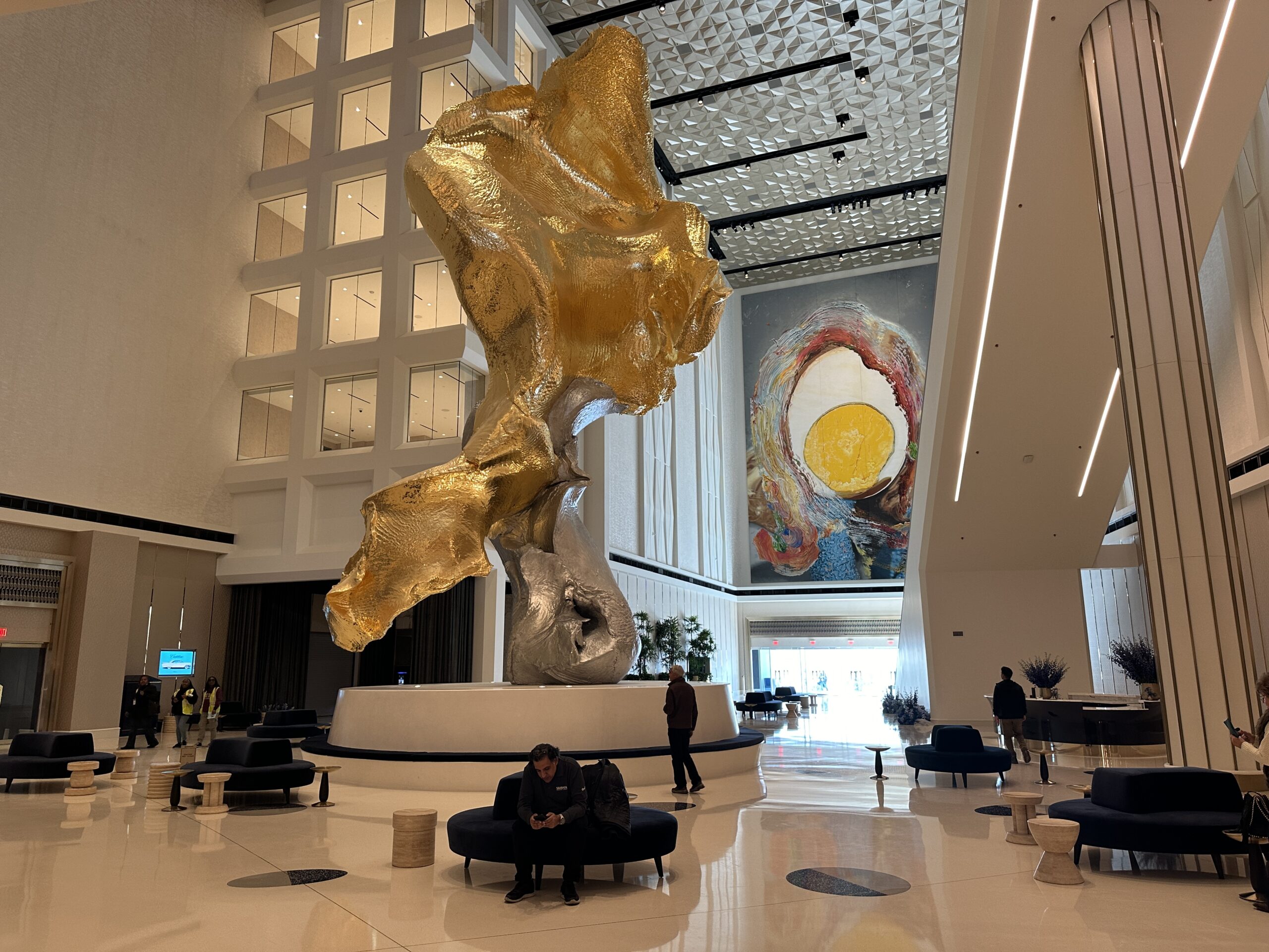 Lovers #3, a 46 foot tall sculpture made of aluminum, steel, and gold stretches toward the ceiling.