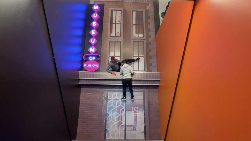 A building facade with a ledge that I am on. The illusion makes it appear my brother fella and I am pulling him back up. 