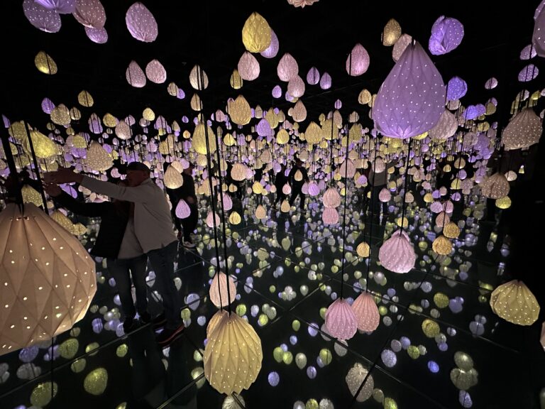 Colorful paper lamps dangle from the ceiling at different hights. Mirrored walls and floors make the "stars" appear to extend into the distance.