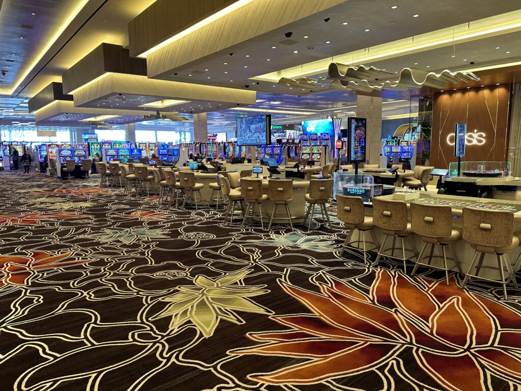 The casino floor at durango. In the foreground is floral patterend carpet and talbe games. In the background are slots as far as the eye can see. 